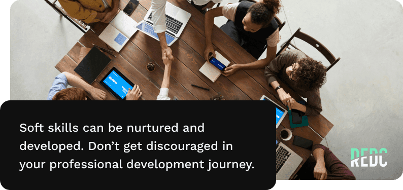 Image: an aerial view of 8 coworkers on laptaops or tablets sitting around a wooden table. Two people are shaking hands across the table. Text: Soft skills can be nurtured and developed. Don't get discouraged in your professional development journey.