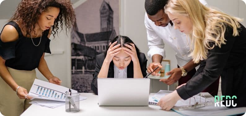 A group working through papers together. One member holds her head in front of a laptop screen.
