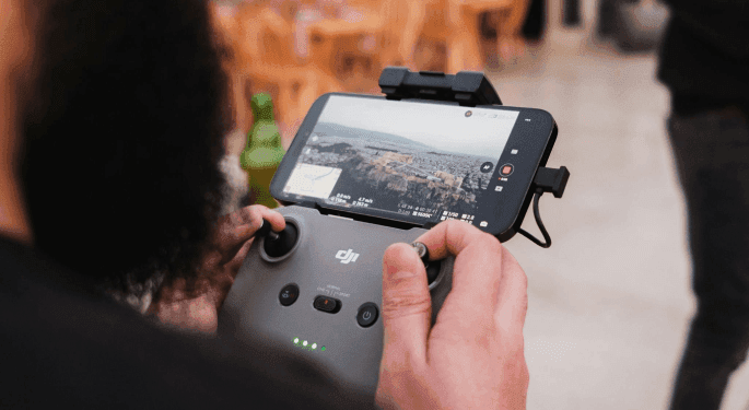 Image: A person holding a drone controller with a phone attached, displaying camera footage from the drone