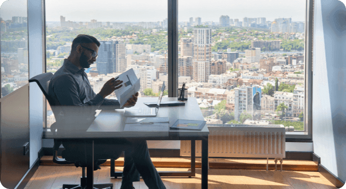 Man in a highrise behind a desk, looking at graphs