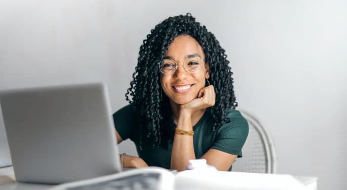 Woman smiling at the camera from behind a laptop.