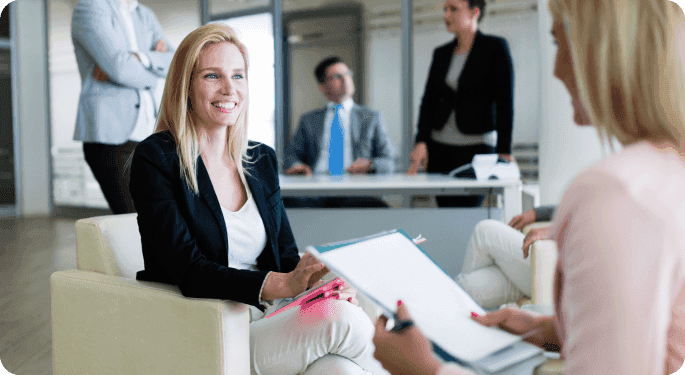 One woman asking another questions from a list in an office setting. 