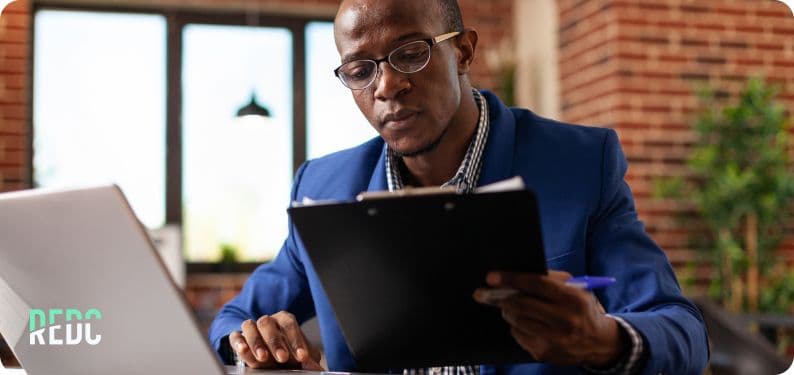 A corporate worker comparing content on his laptop and clipboard. 