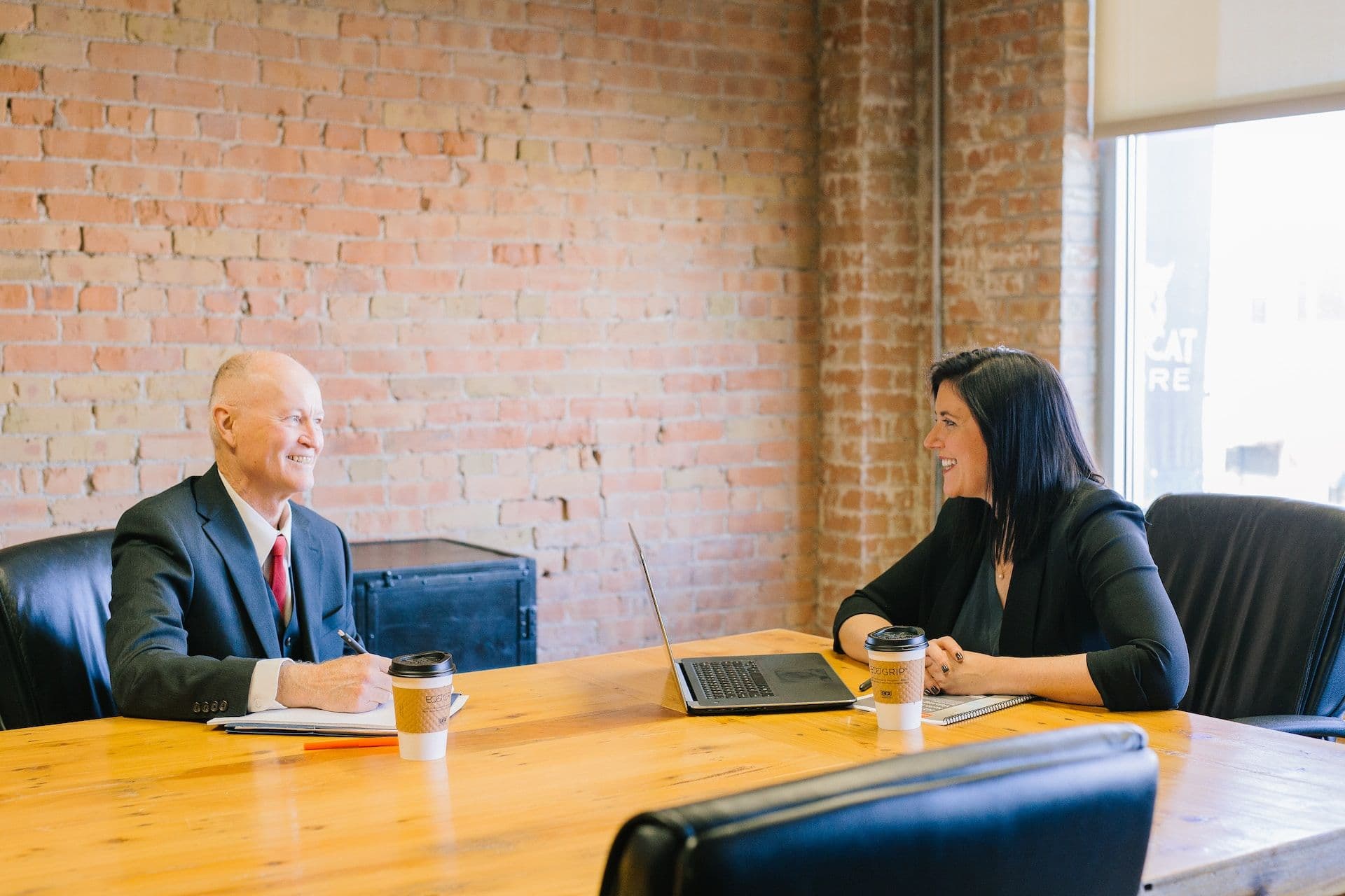 Elderly man sits with younger woman at business table