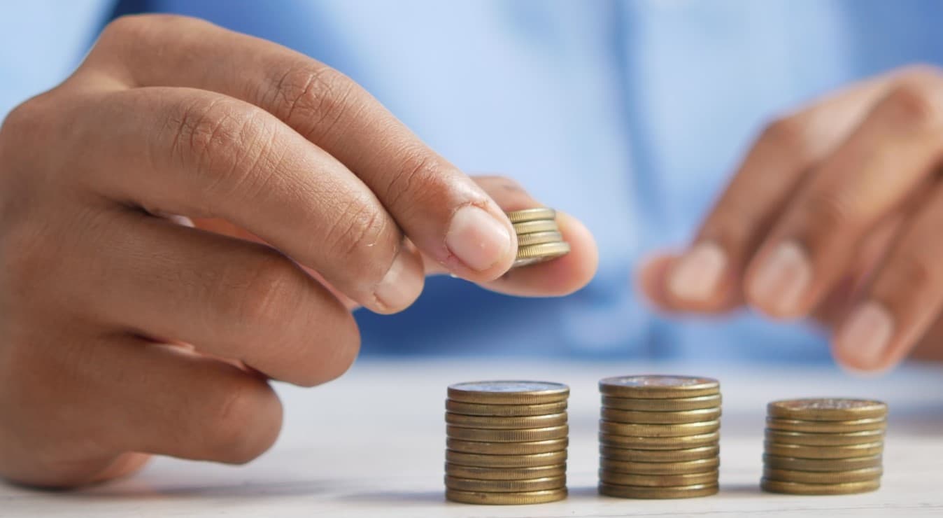 A person meticulously counts a stack of coins on a wooden table, carefully organizing and tallying their monetary value.