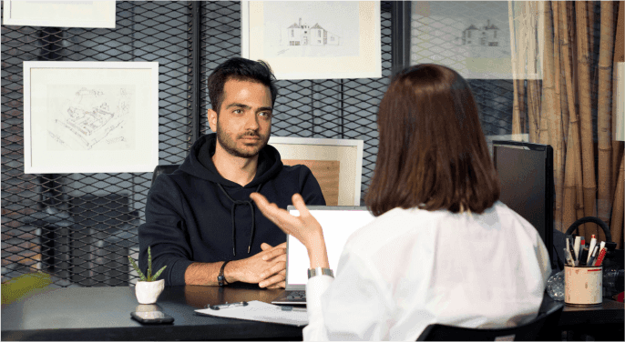 Image: A job-seeker sitting across a desk from an interviewer in a fancy office.