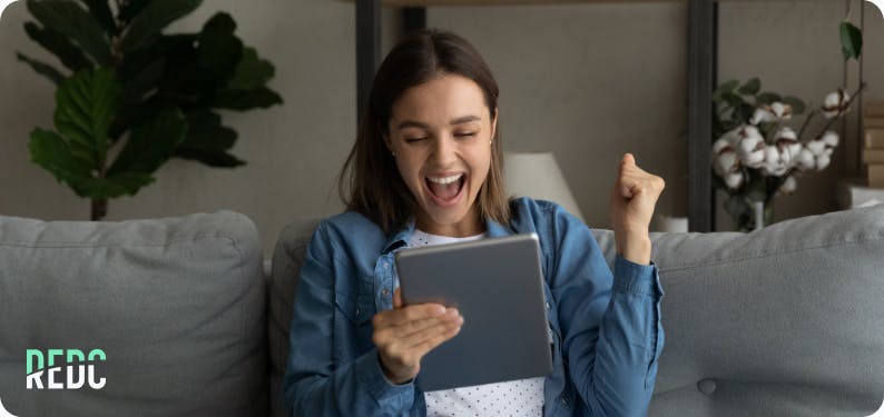 A woman smiling and fist pumping while looking at a tablet.